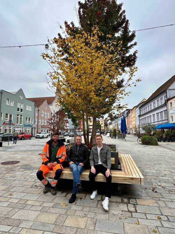 Bürgermeister Armin Grassinger (Mitte), Christoph Aigner von der Stadtgärtnerei und Klimaschutzmanager Stefan Salzinger testen eine der Sitzbänke an den neuen Bauminseln.